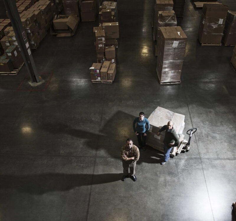 A group of three warehouse workers standing in the center of a distirbution warehouse.